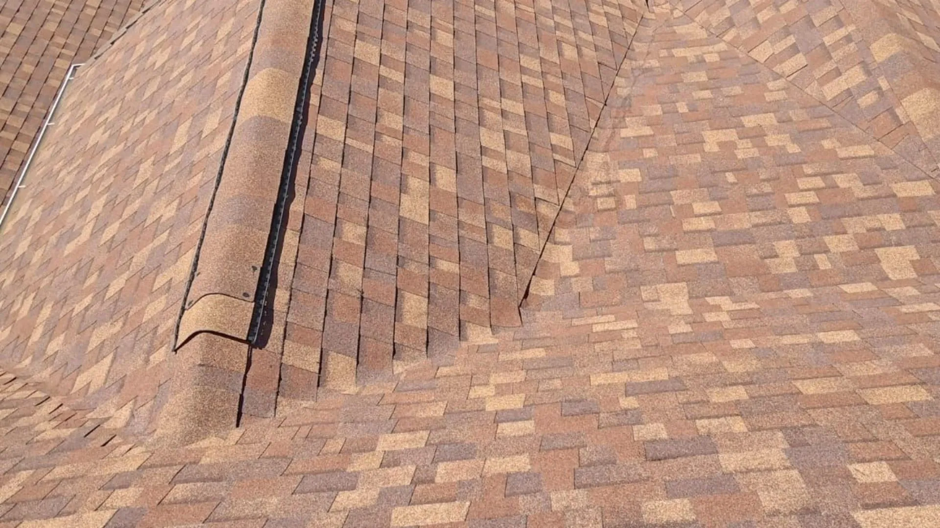 A roof with light gray shingles and multiple vent pipes, set in a residential neighborhood with green lawns and parked cars.